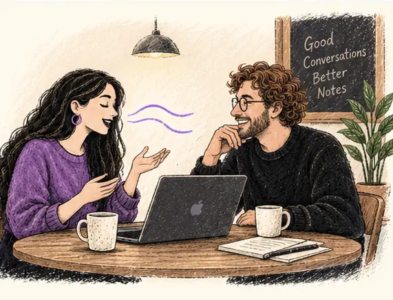 Two people talking across a café table with a Mac between them.